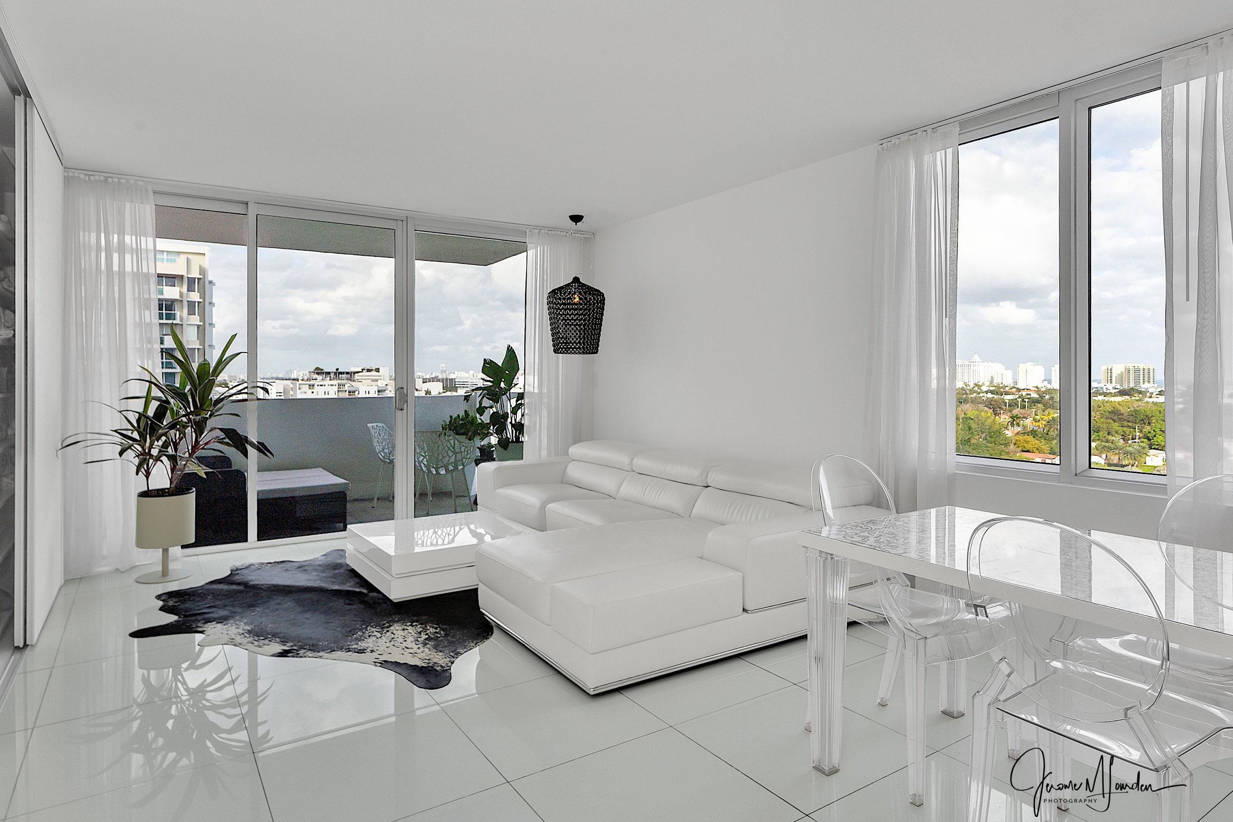 Ultra-white living room with white leather sectional, balcony, city views, and tropical plants